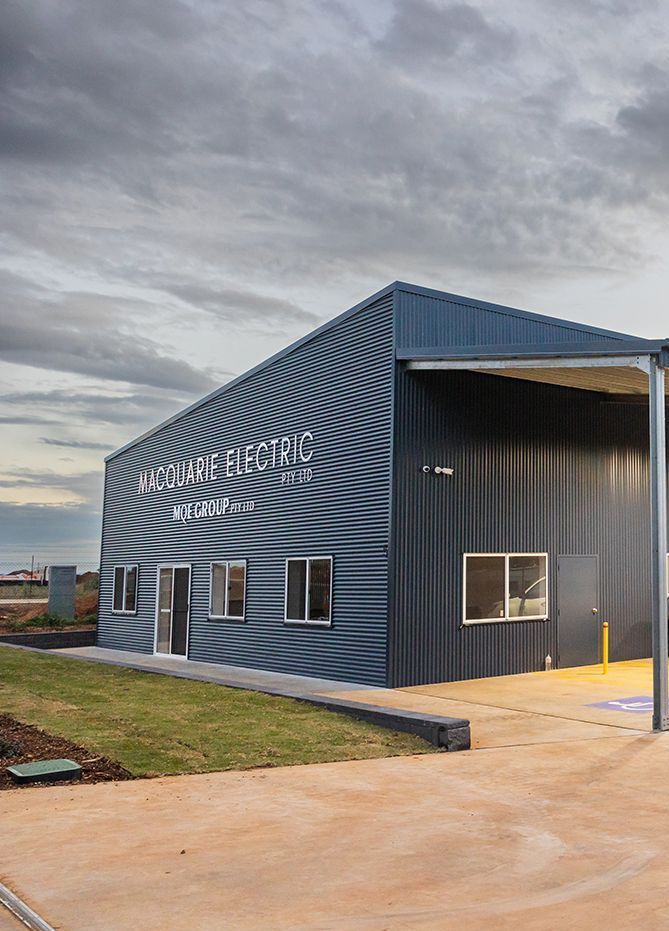 A Man in an Orange and Blue Safety Vest is Working on an Electrical Box — Macquarie Electric in Dubbo, NSW