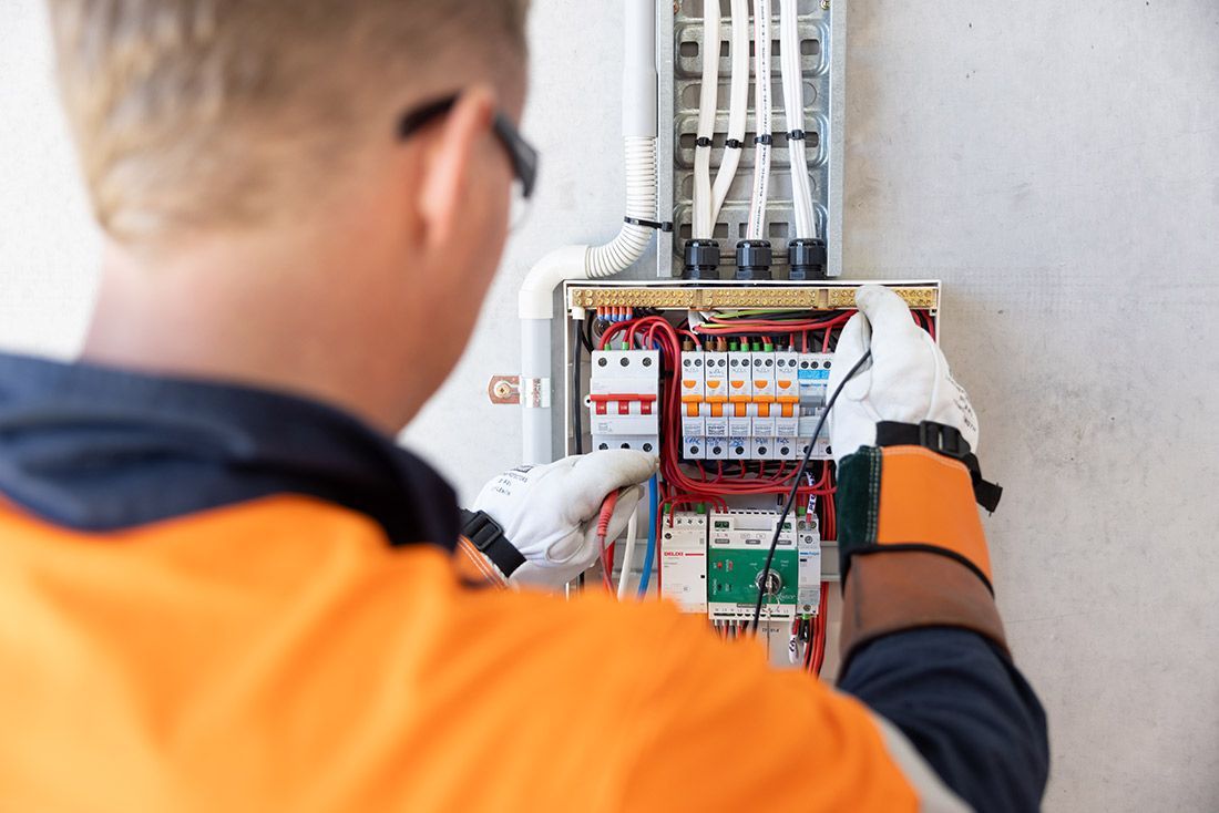 A Man in an Orange Shirt is Working on an Electrical Box — Macquarie Electric in Wellington, NSW
