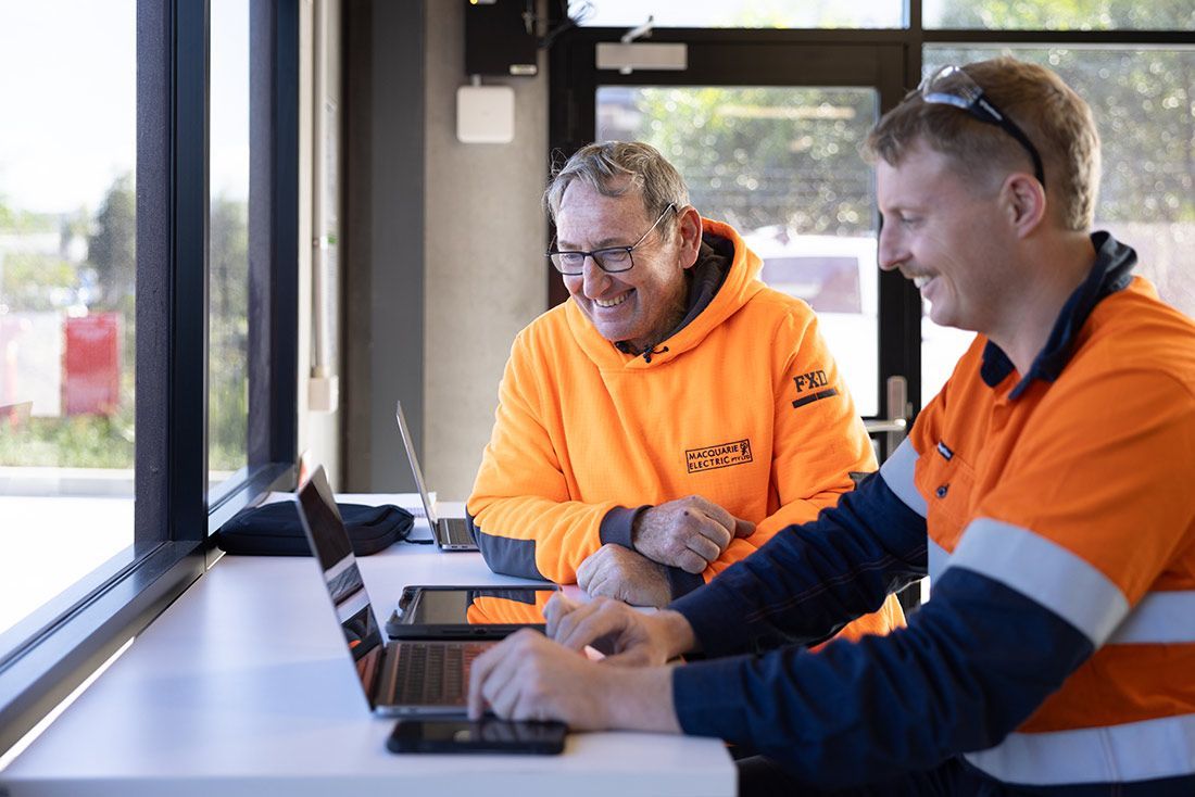Two Men Are Sitting at a Table Looking at a Laptop — Macquarie Electric in Mudgee, NSW