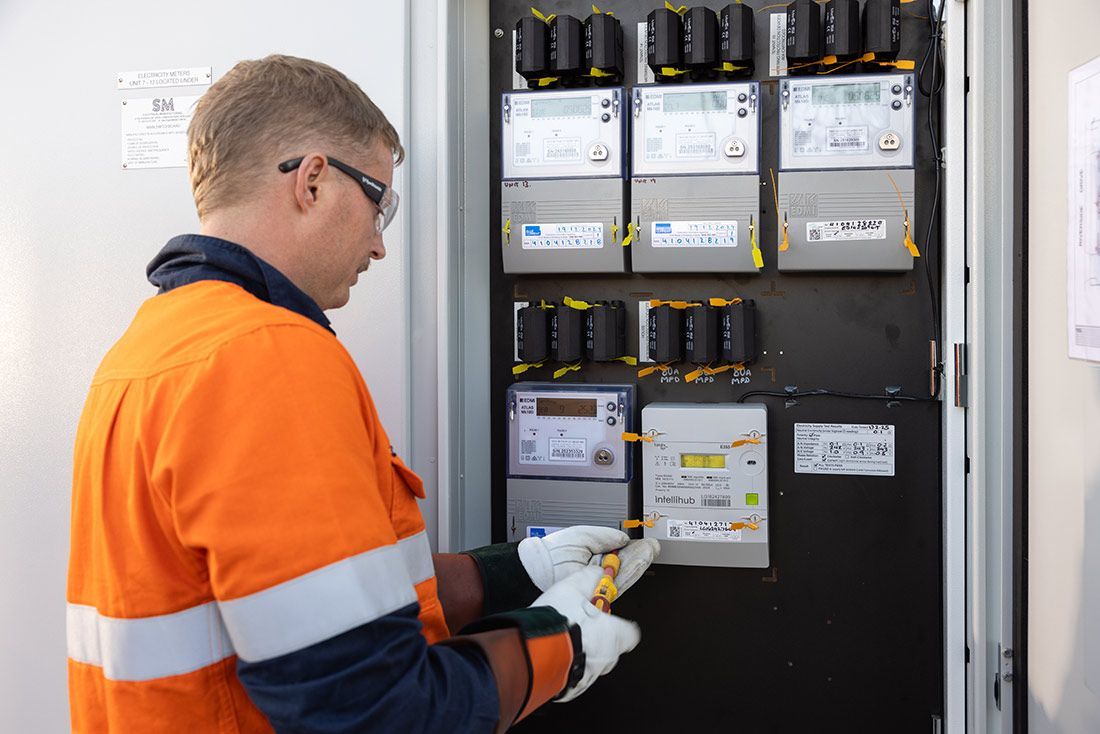 A Man in an Orange and White Safety Vest is Working on an Electrical Box — Macquarie Electric in Sydney, NSW