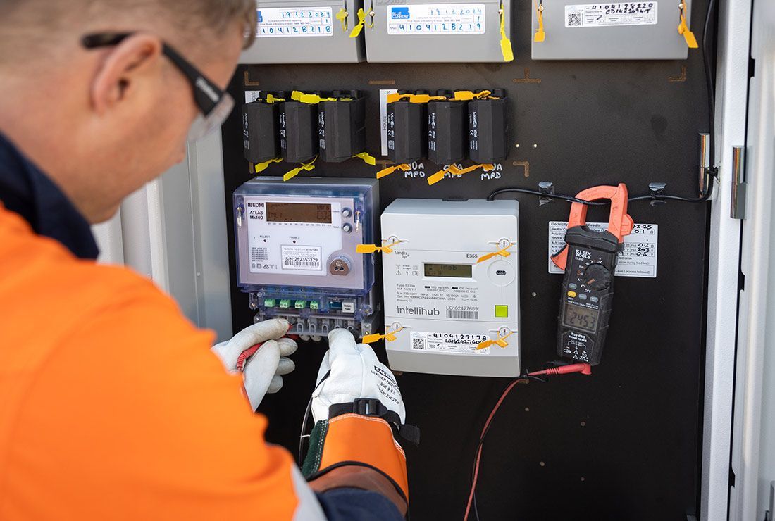 A Man in an Orange Shirt is Working on an Electrical Box — Macquarie Electric in Dubbo, NSW
