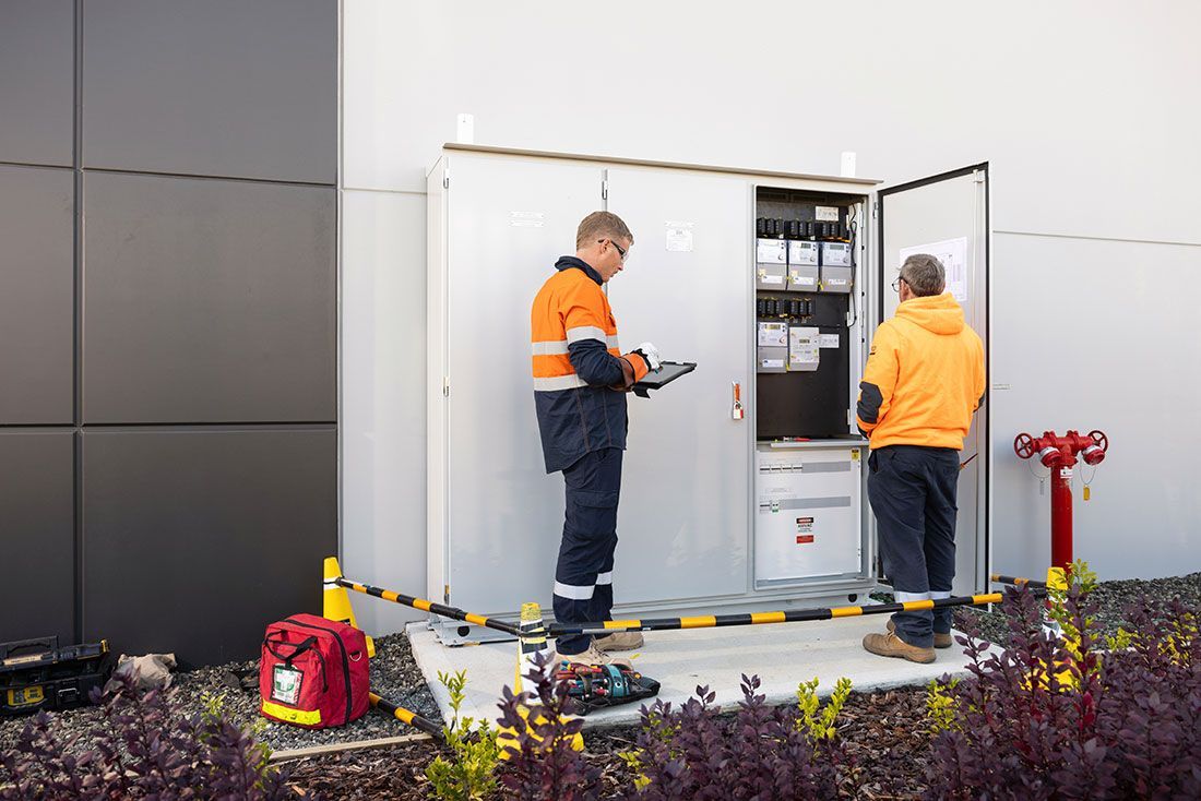 Two Men Are Working on a Electrical Box Outside of a Building — Macquarie Electric in Wellington, NSW