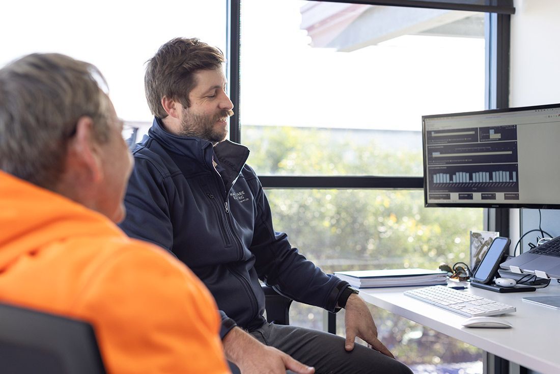 Two Men Are Sitting at a Desk in Front of a Computer Monitor — Macquarie Electric in Adelaide, SA