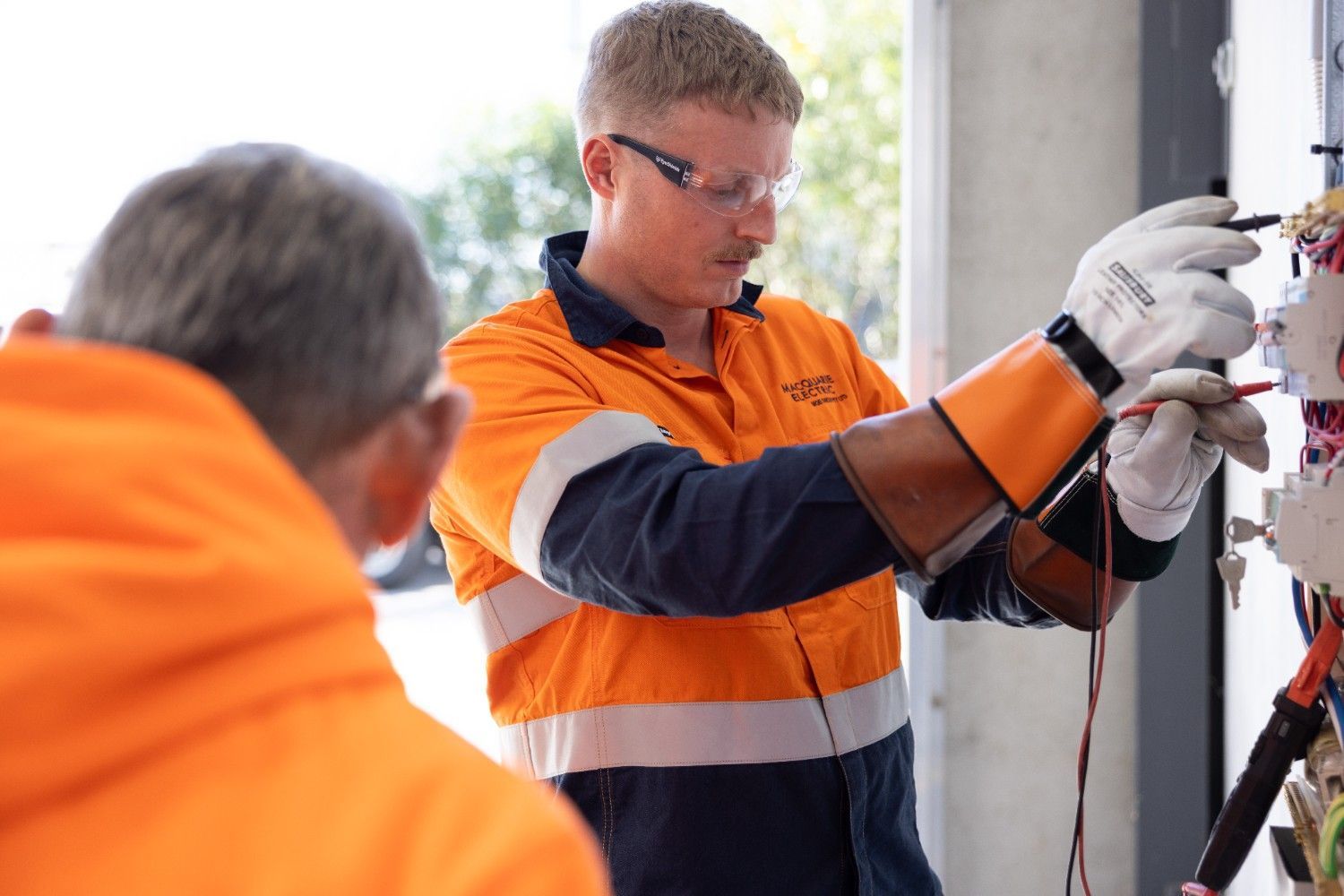 A Man in An Orange Jacket Is Working on A Wire While Another Man Watches — Macquarie Electric in Newcastle, NSW