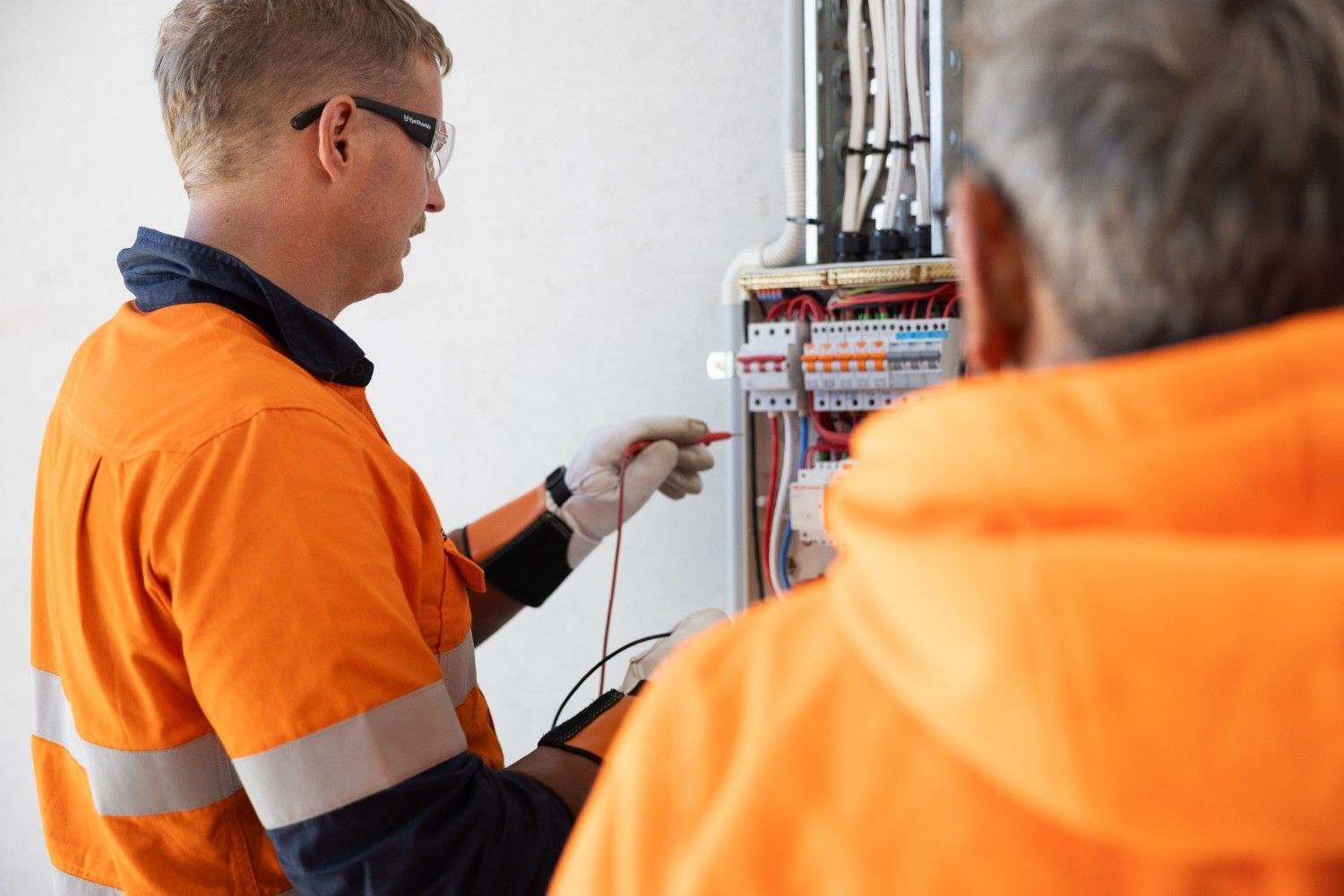 Two Men in Orange Safety Jackets Are Working on An Electrical Box — Macquarie Electric in Newcastle, NSW