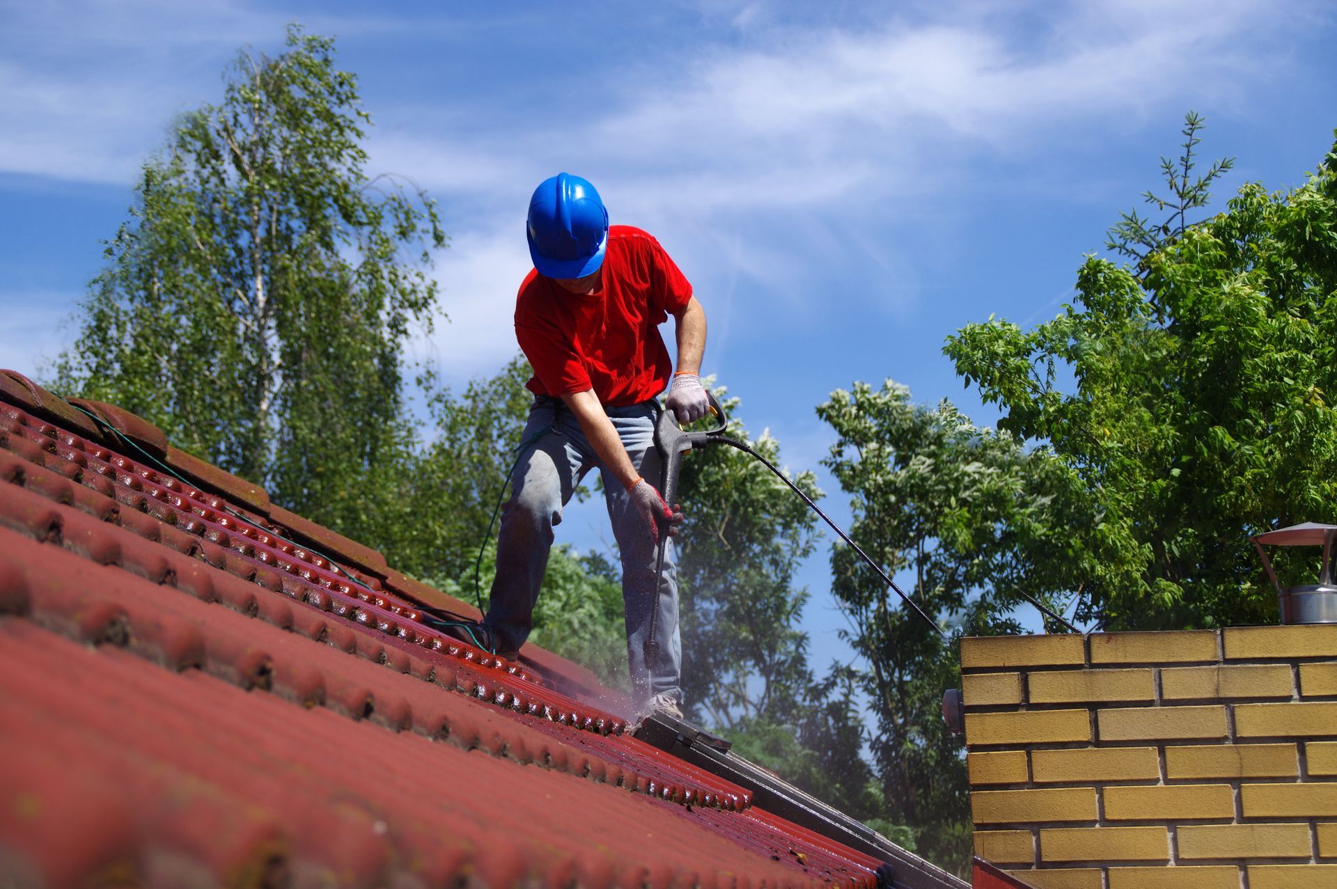 A man is cleaning the roof of a house with a high pressure washer.