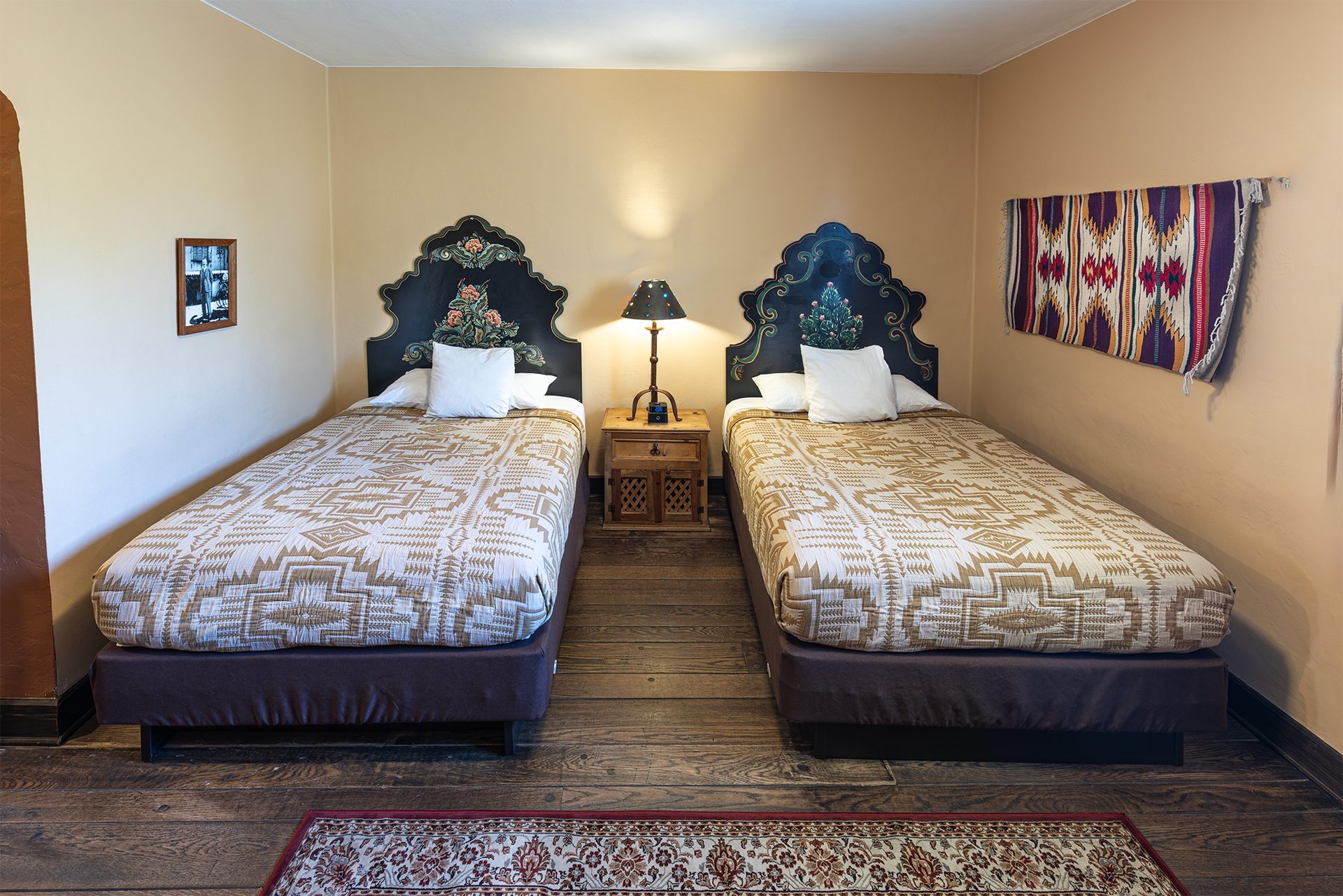 Two twin beds with ornate headboards, nightstand, and woven rug in a bedroom.
