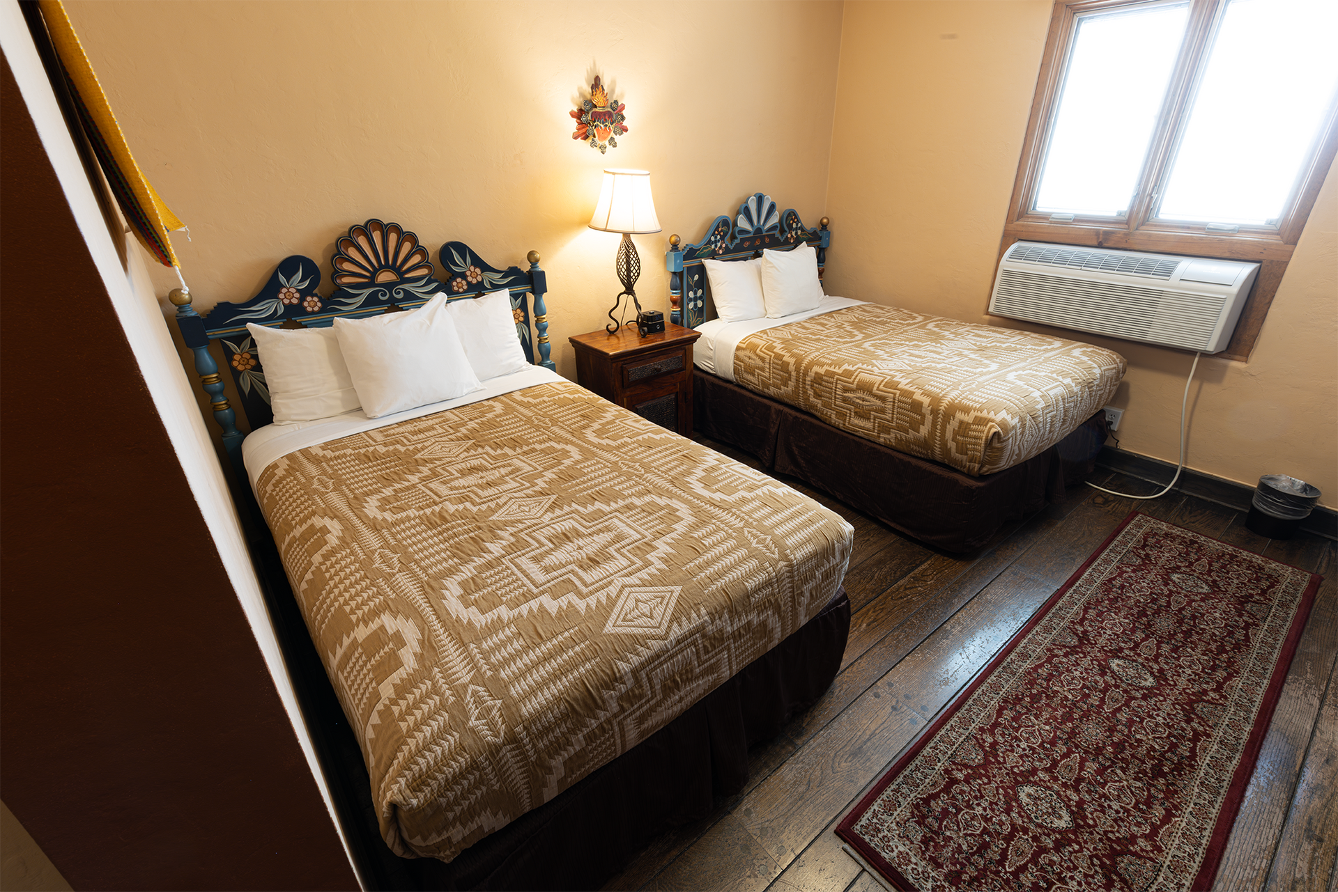 Two twin beds in a hotel room with patterned bedspreads and a small rug.