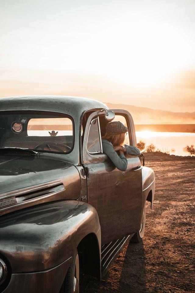 A sunset photo of an old truck with a girl looking out the window