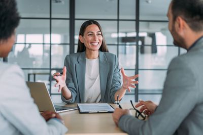 Una mujer está sentada en una mesa hablando con un grupo de personas.