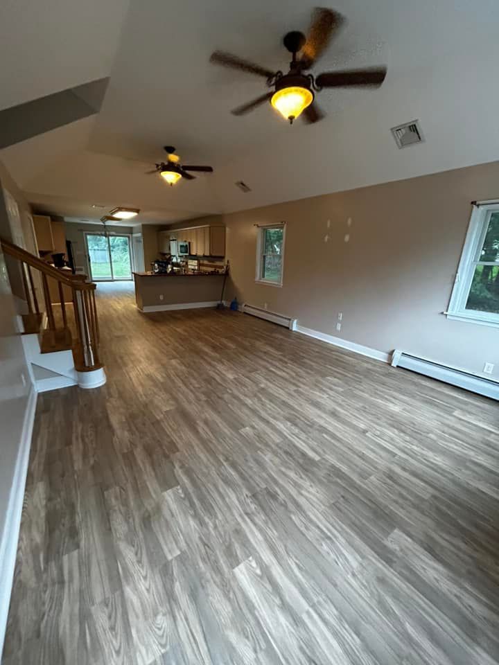 Living room with wood-look flooring, tan walls, two ceiling fans, and a view of the kitchen.