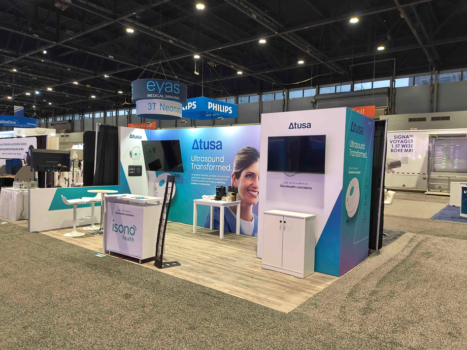 Trade show booth with white and teal accents, featuring screens and brand logos.