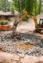 A yellow excavator breaks apart a concrete swimming pool in a residential backyard while two workers observe.