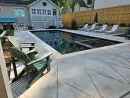 A backyard patio with two green chairs in the foreground, overlooking a rectangular swimming pool with an attached spa.