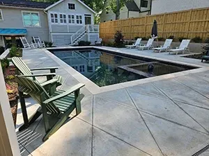 A backyard patio with two green chairs in the foreground, overlooking a rectangular swimming pool with an attached spa.