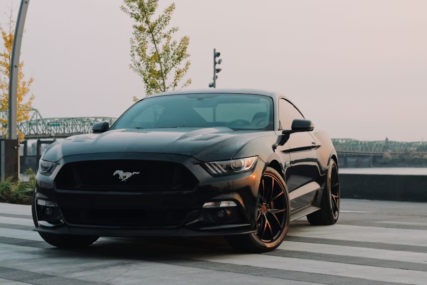 Black Ford Mustang parked outdoors, sunset lighting.