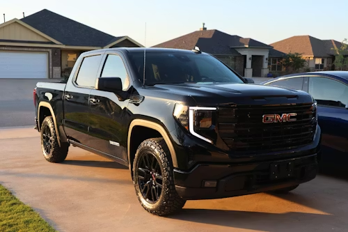 A black GMC Sierra pickup truck parked on a residential driveway in front of suburban houses.