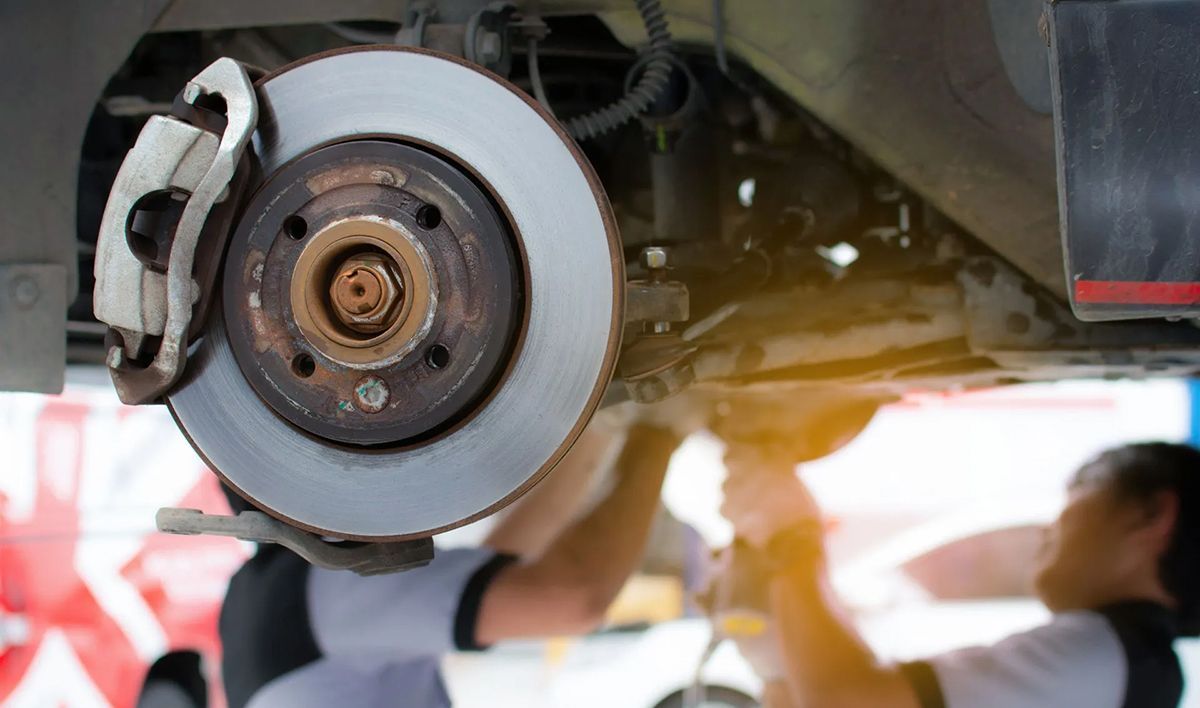 Car brake assembly with mechanics working underneath, close-up.