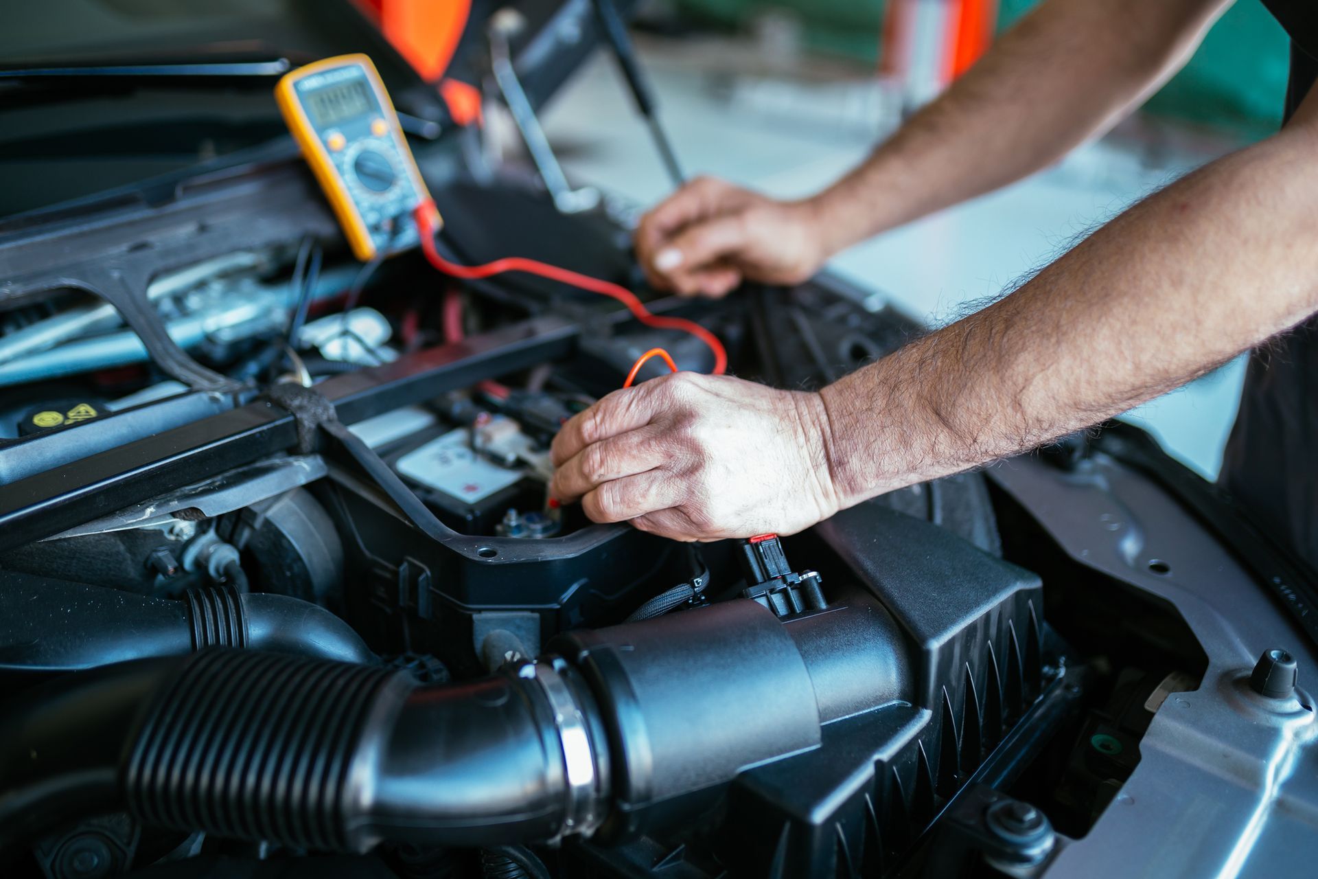 A man is working on the engine of a car with a multimeter.