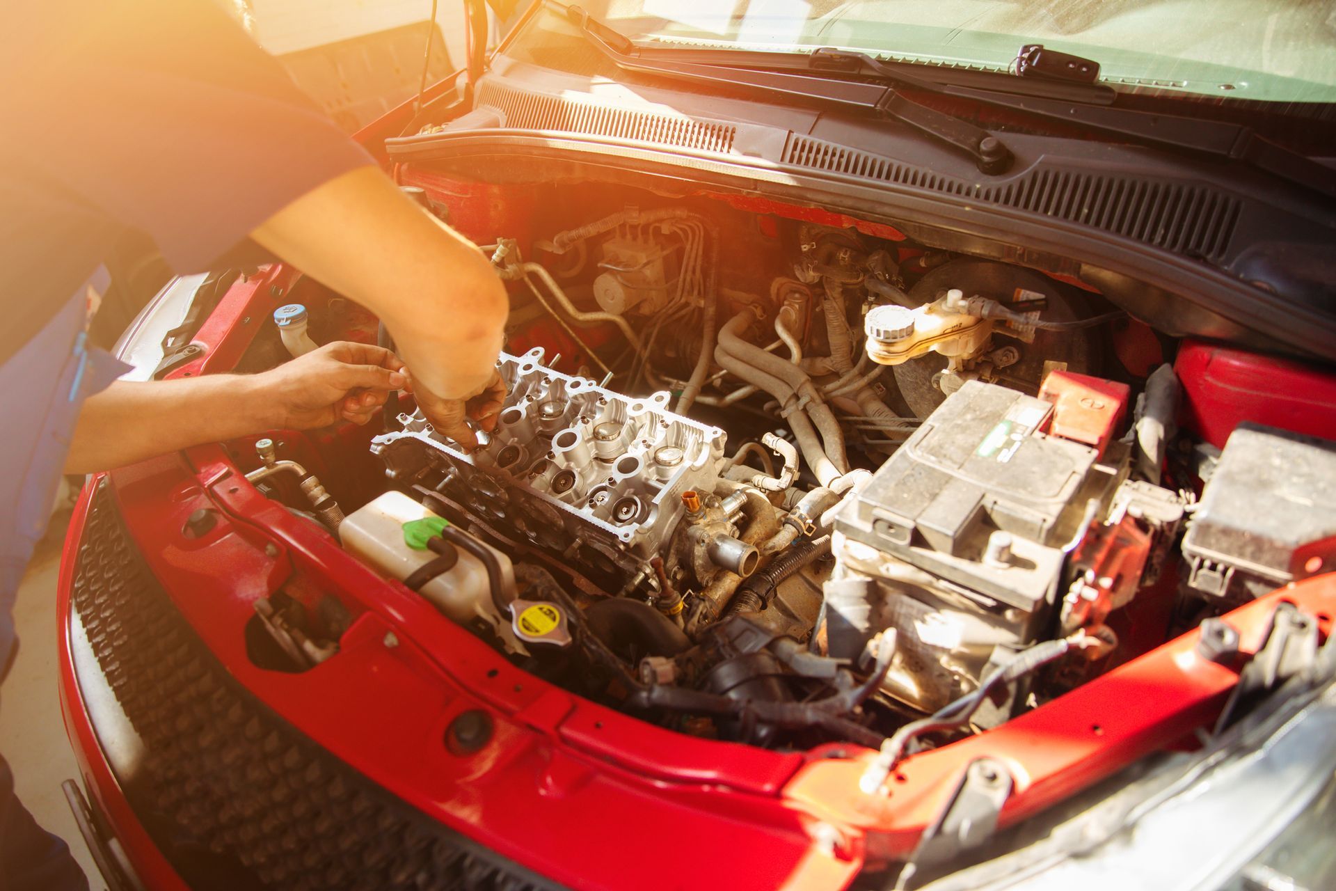 A man is working on the engine of a red car.