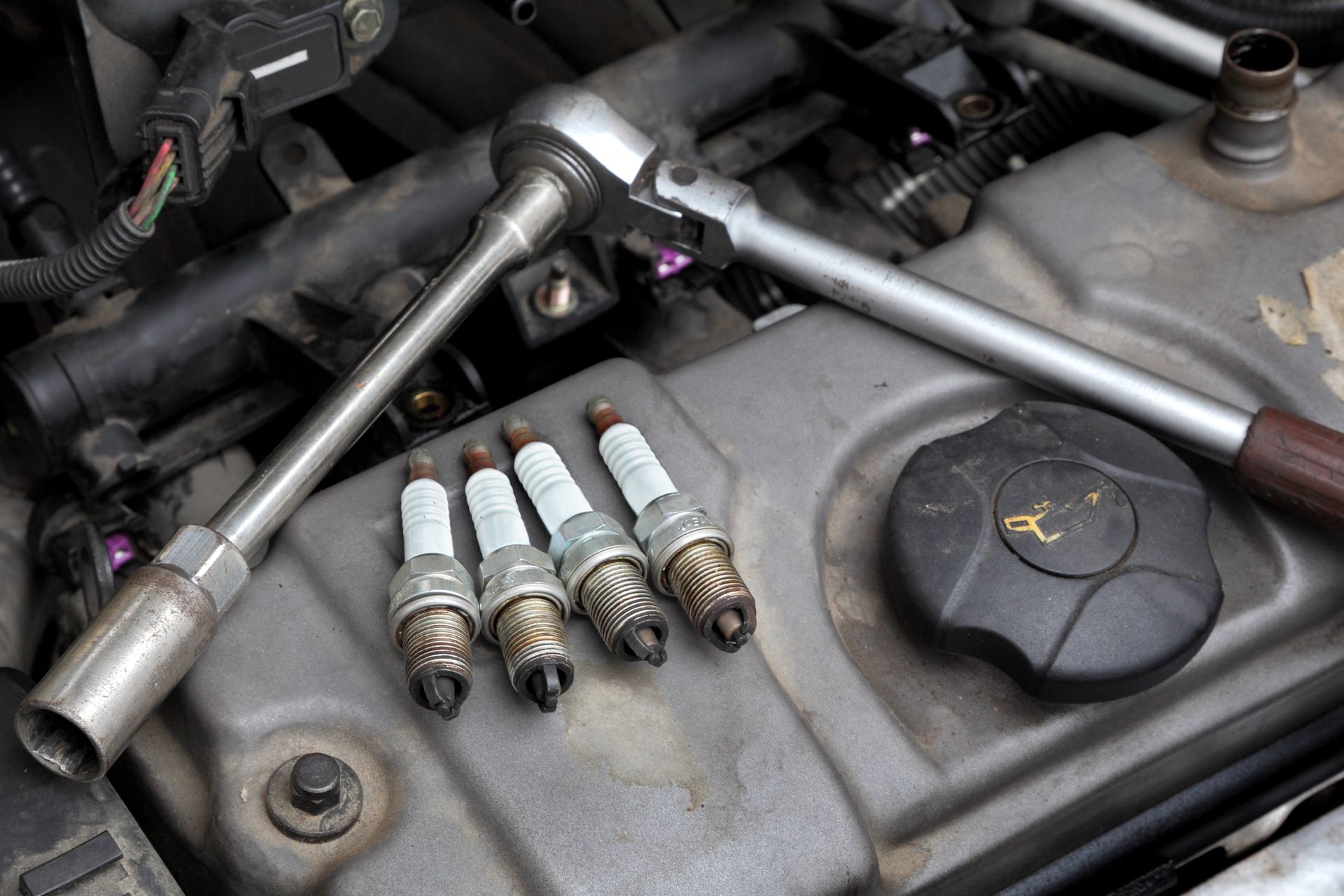 A close up of a car engine with spark plugs and a wrench.