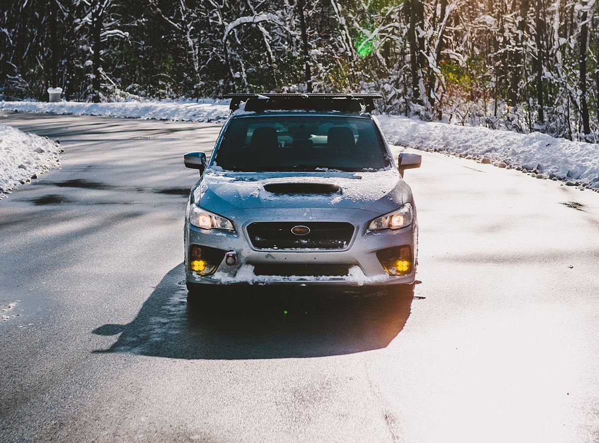 A silver car is driving down a snowy road.
