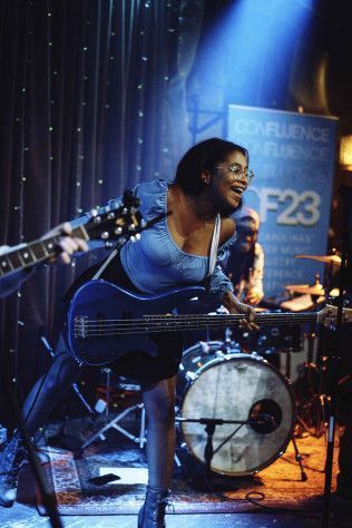 A person plays a blue bass guitar on a dimly lit stage during a live performance in front of a blue