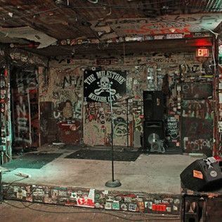 The Milestone Club stage, featuring graffiti-covered walls, a microphone stand, and a black speaker.