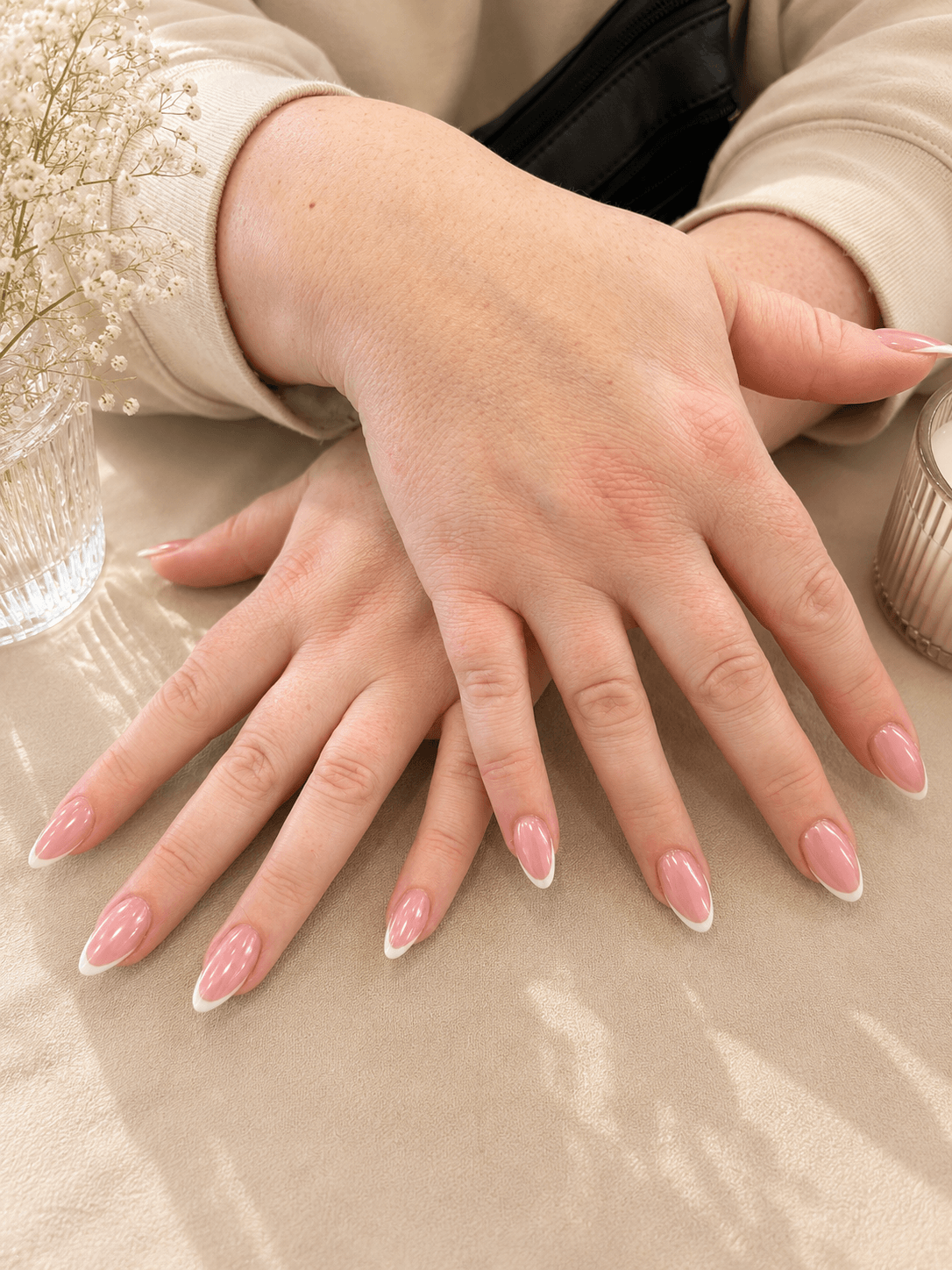 Hands with pink glittery manicure resting on a beige satin surface.
