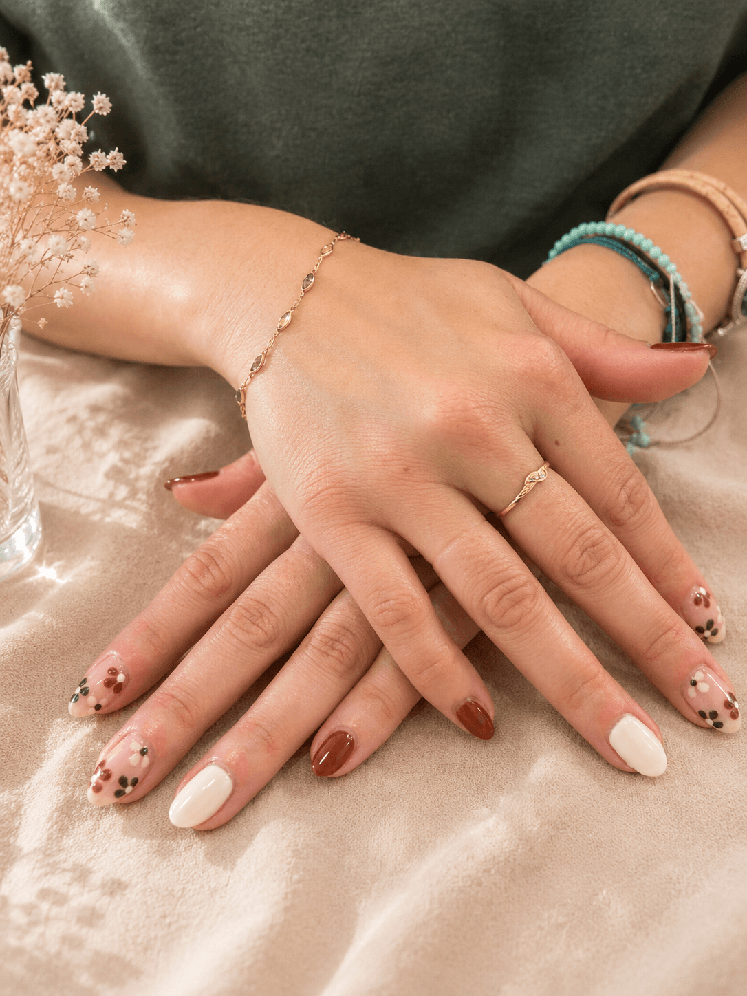 Interlaced hands with nude and floral manicured nails on a satin fabric backdrop