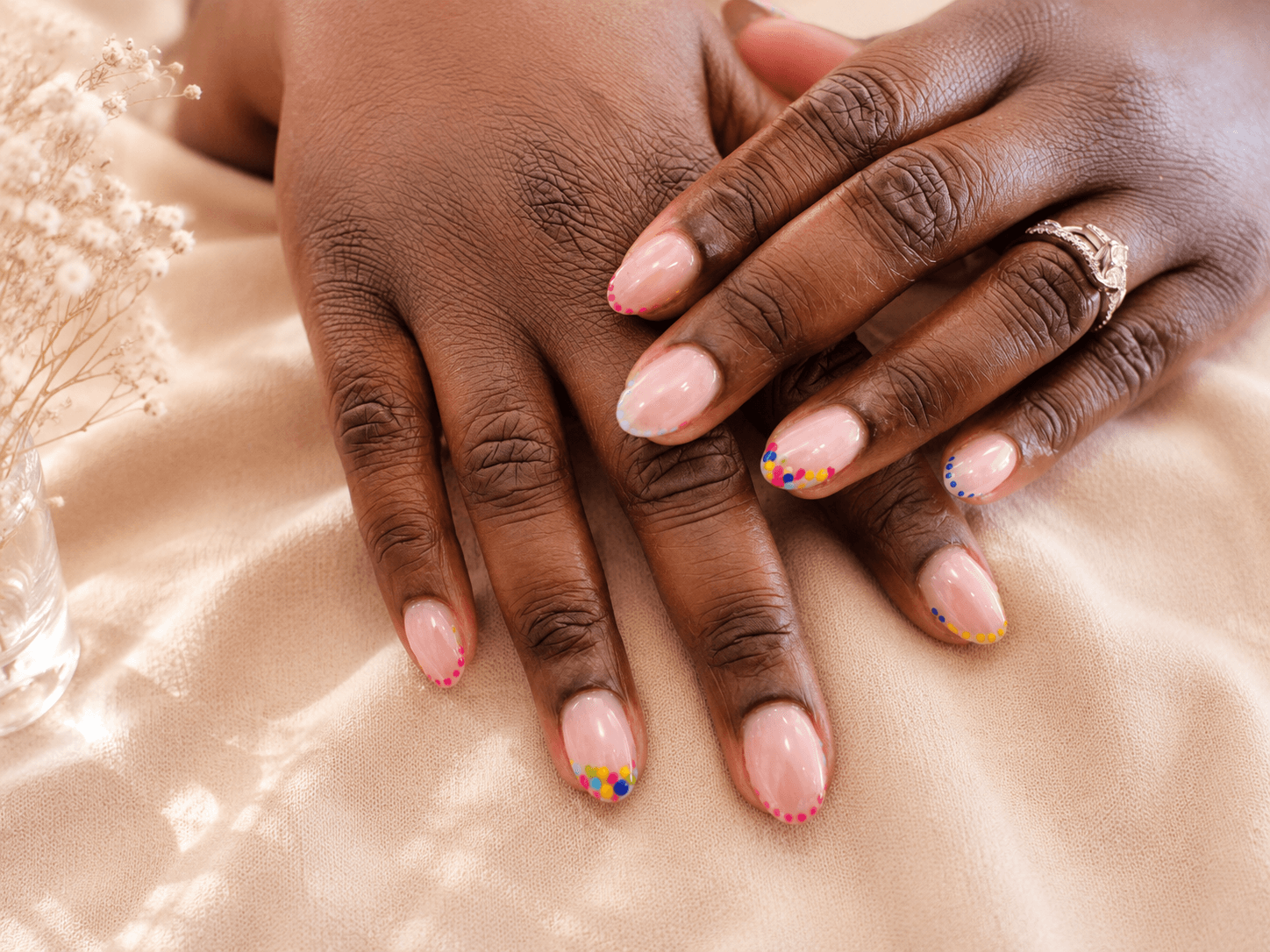 Hands with French manicure and gold ring resting on a silky beige fabric.