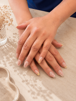 Hands with pale pink manicured nails resting on a lace-covered table.