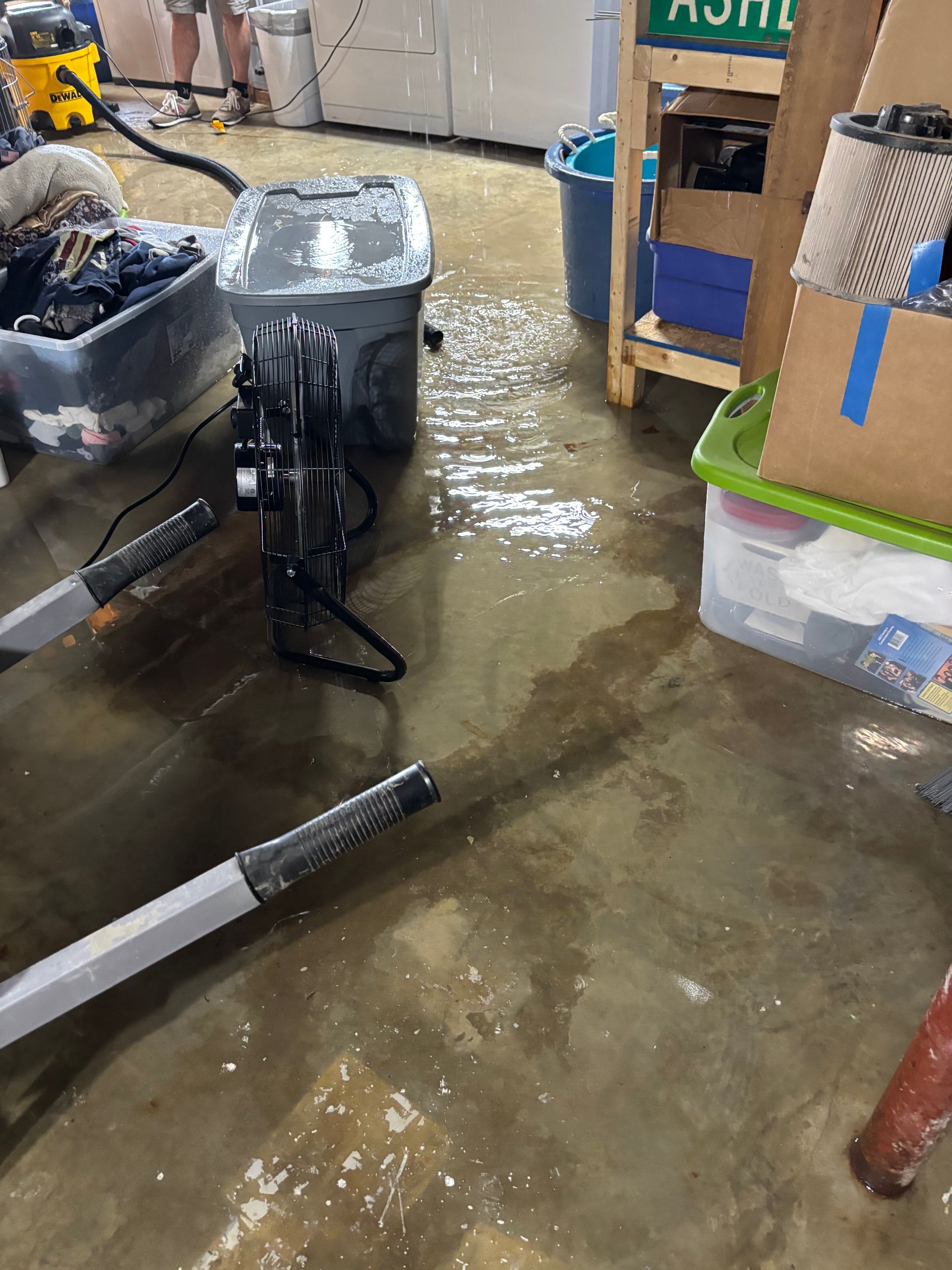 Wet warehouse floor with a standing fan, boxes, and tools scattered around.