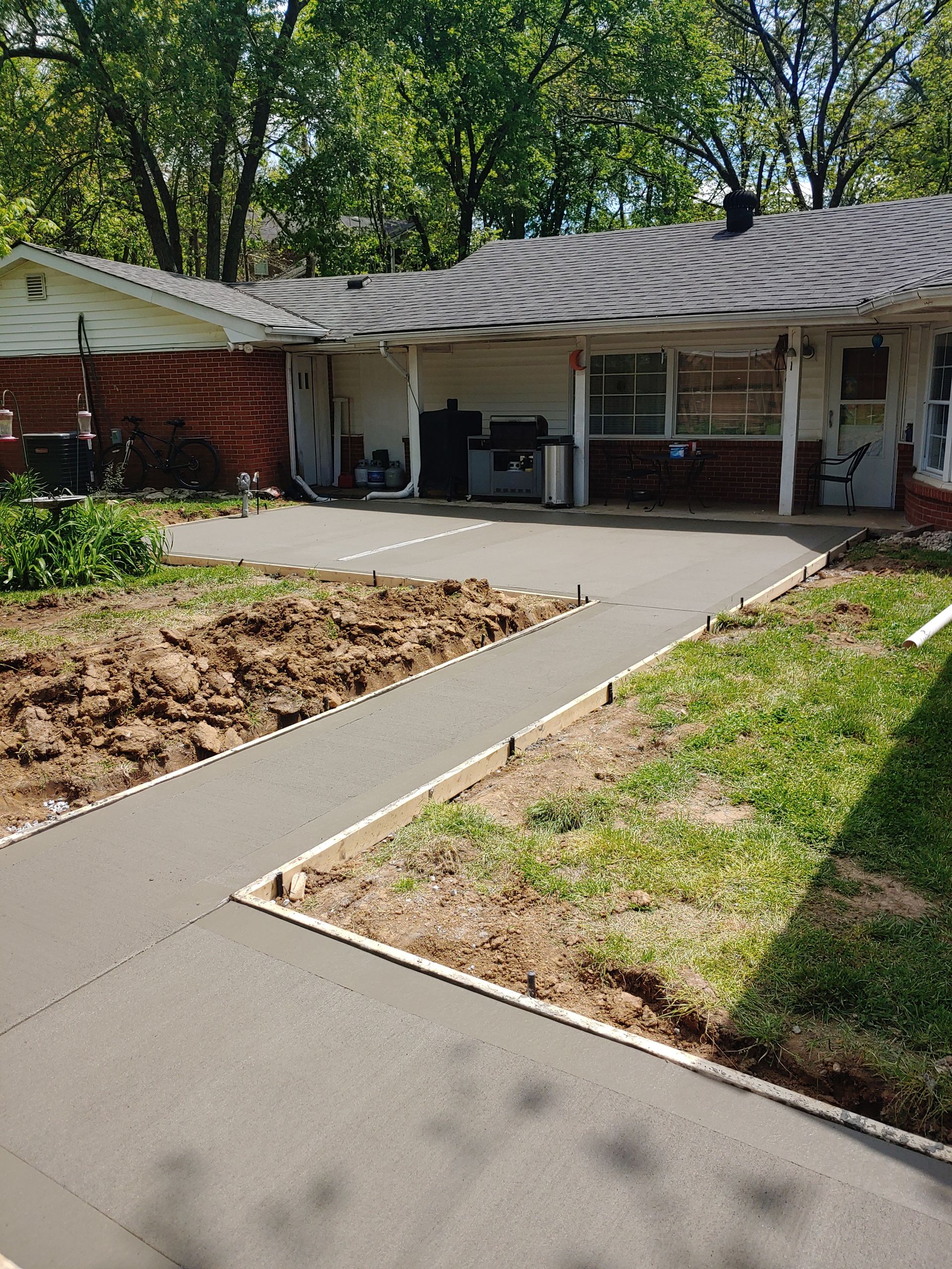 Concrete walkway leading to a brick house with a covered porch and trees in the yard