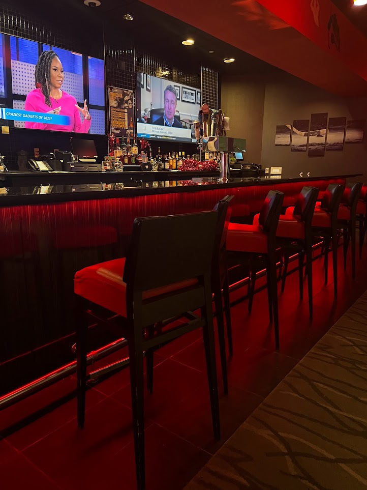 Red-lit bar with stools and two TVs showing a news broadcast.