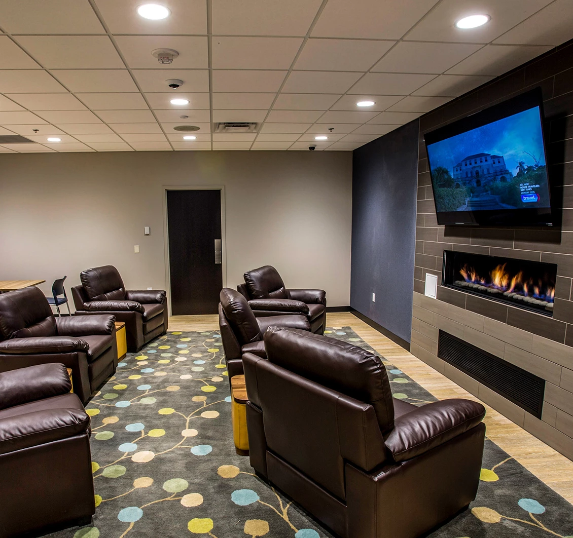 Modern lounge with leather chairs, a fireplace, wall-mounted TV, and patterned carpet