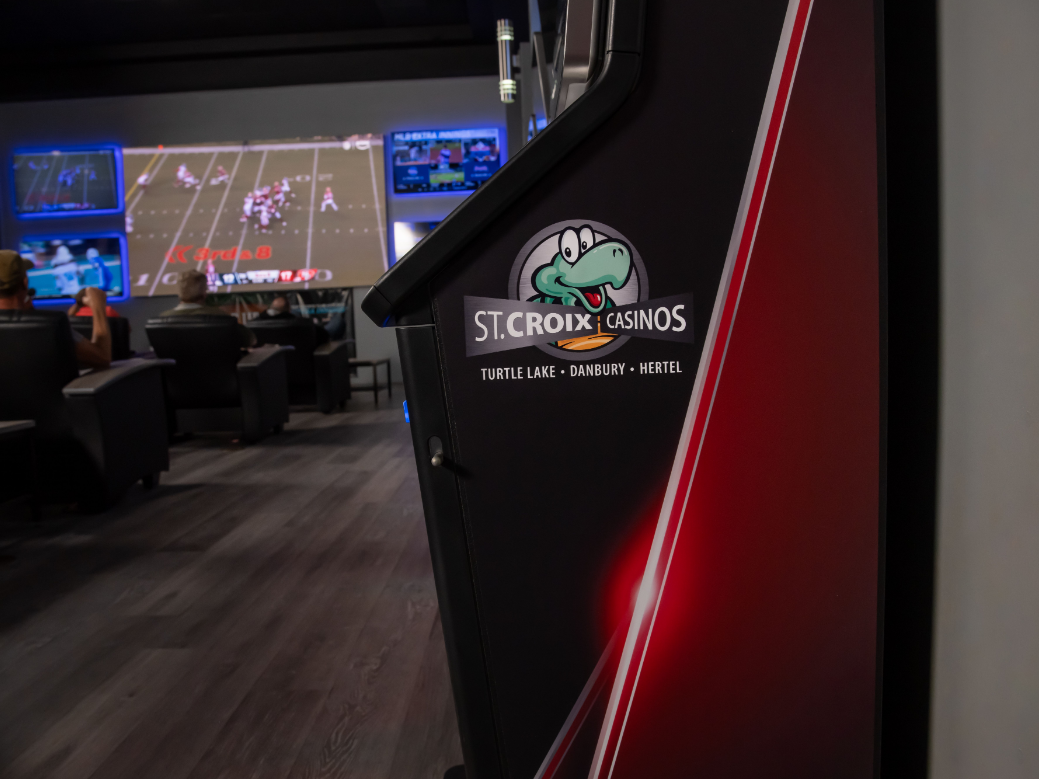 Casino interior with poker tables, gaming screens, and a red-lit St. Croix 3605 cabinet in the foreground