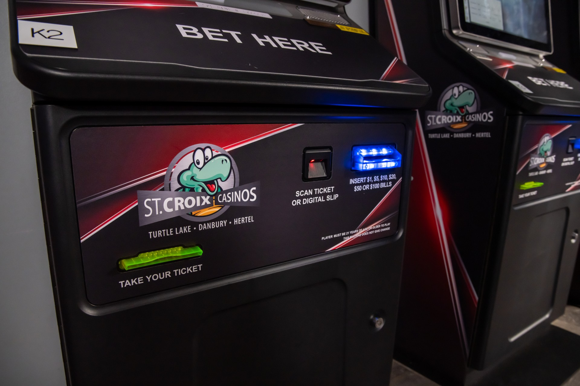 Row of black video slot machines with glowing screens and “Bet Here” signs in a casino