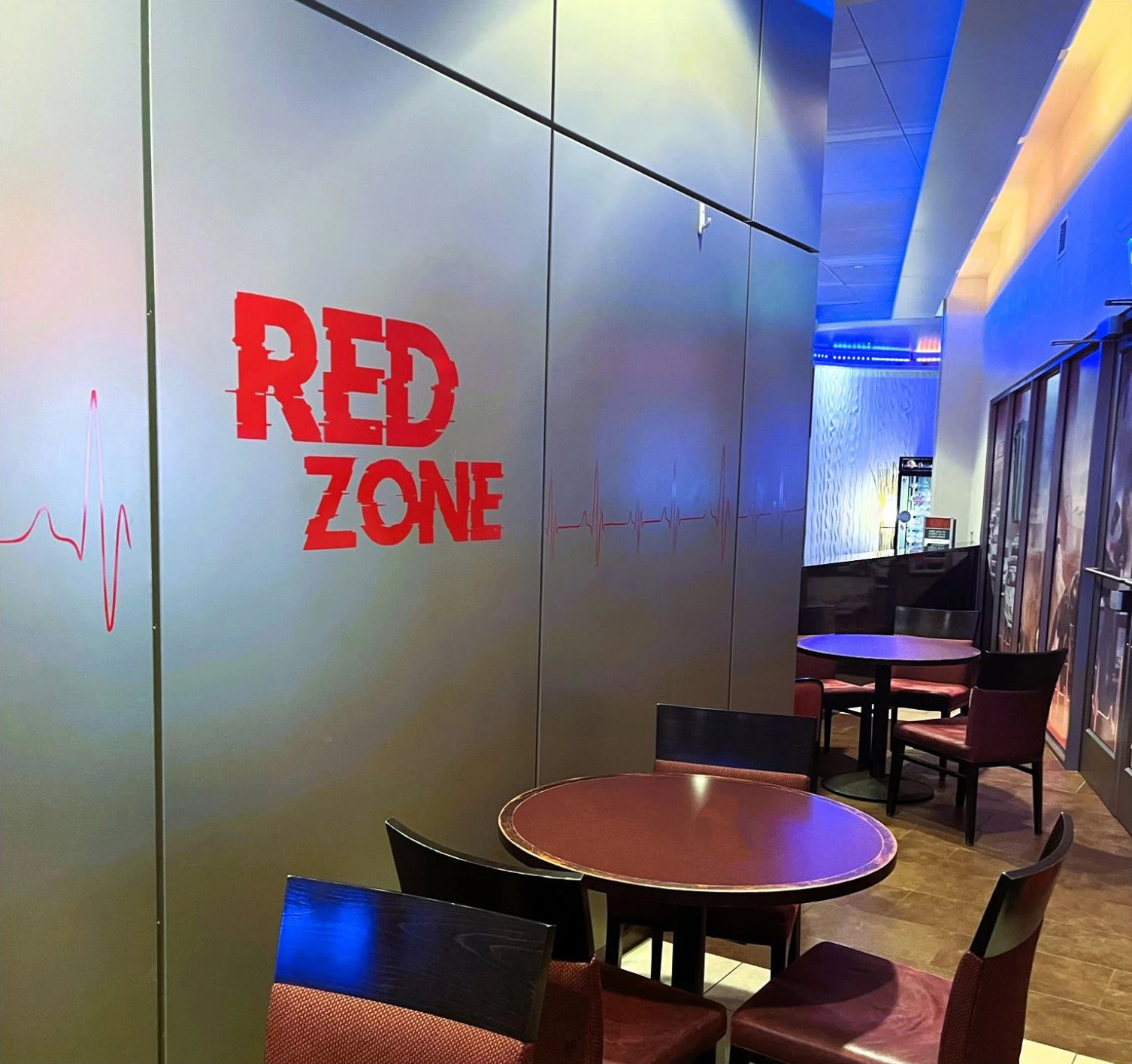 Dim restaurant interior with red “RED ZONE” lettering on a wall beside tables and chairs.