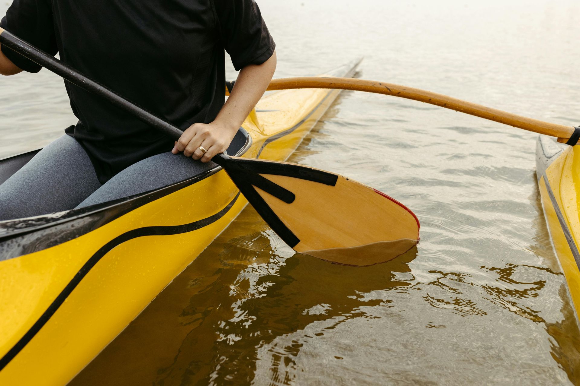 Person paddling a yellow kayak on brown water