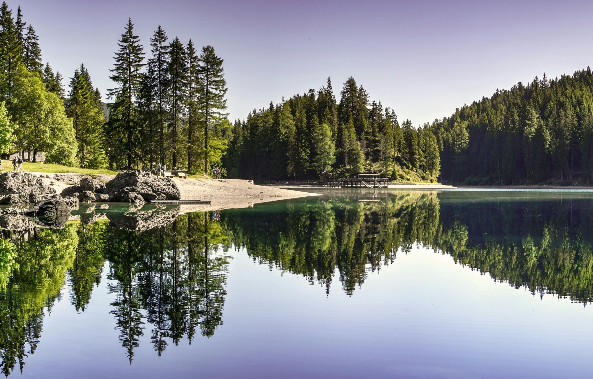 Calm forest lake reflecting evergreen trees and a rocky shore under a clear sky