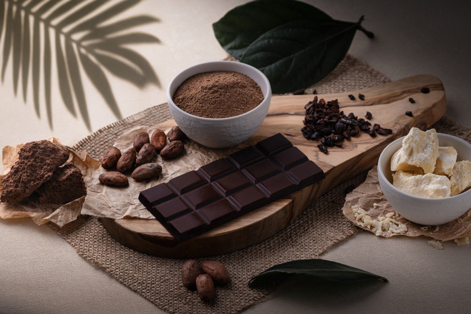 A wooden cutting board with a bar of chocolate and a bowl of cocoa powder