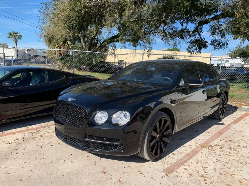 Black Bentley parked in a lot next to a black sports car on a sunny day.