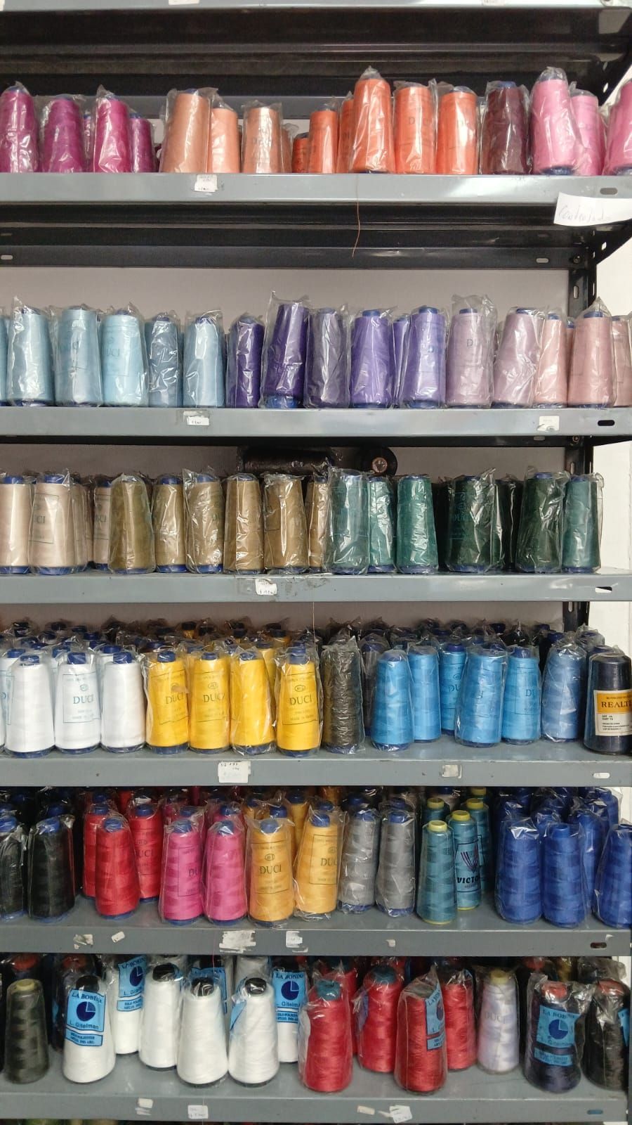 Estantes repletos de carretes de cinta o hilo de colores, ordenados con esmero, en el escaparate de una tienda.