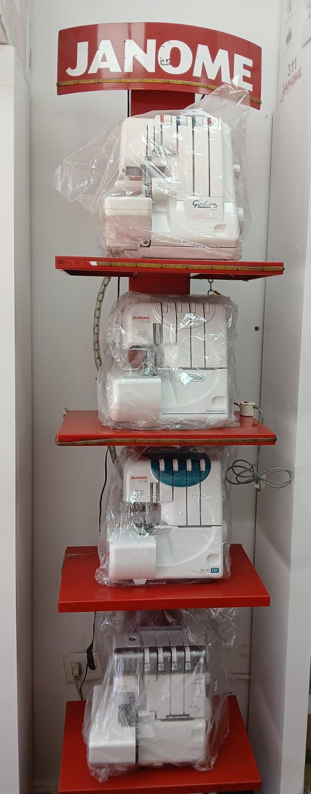 Exhibición de máquinas de coser Janome en estantes rojos en una tienda.