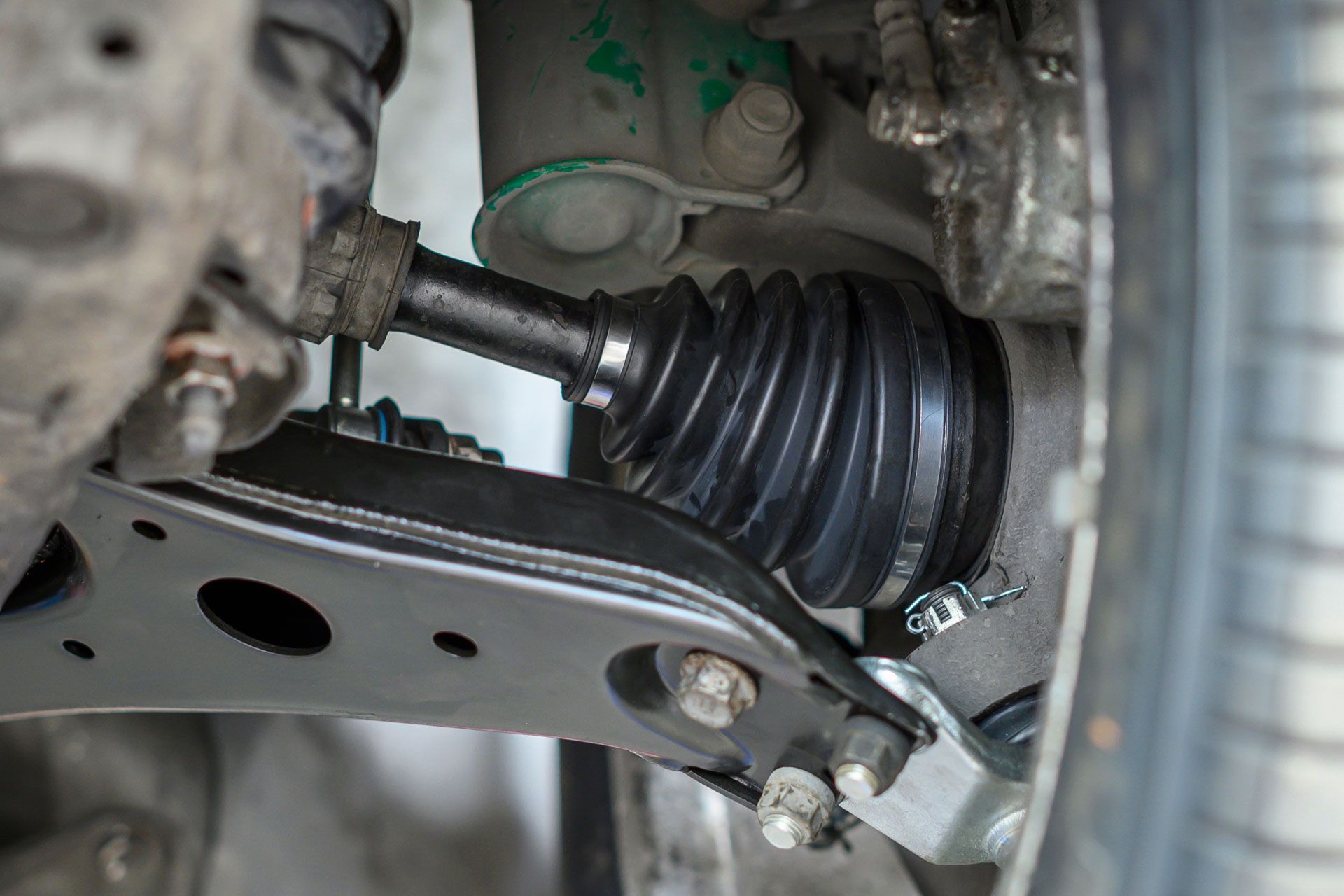 Close-up of a car CV axle with black rubber boot and suspension parts underneath.