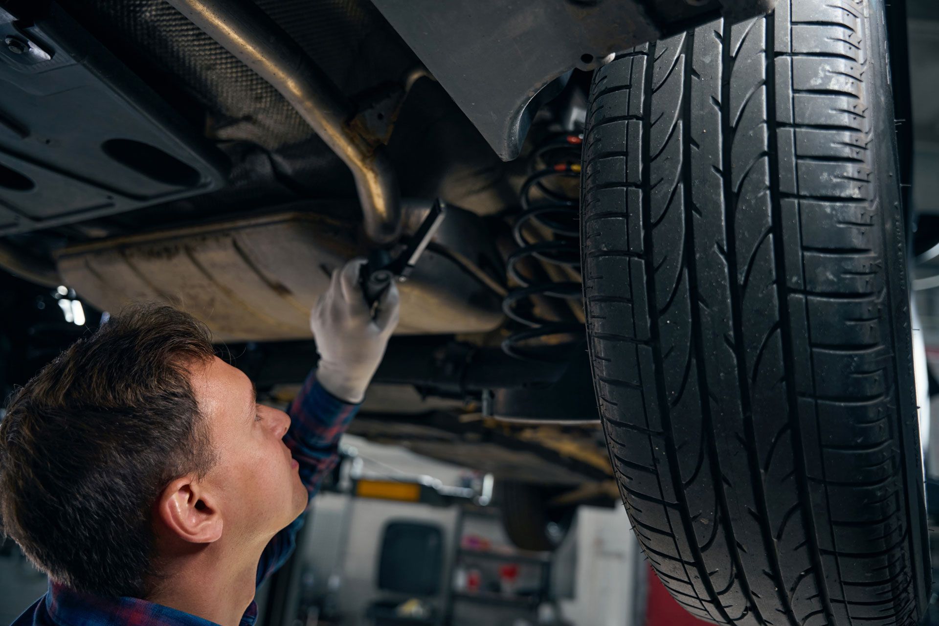 Mechanic inspecting the underside of a car beside a front tire in a garage