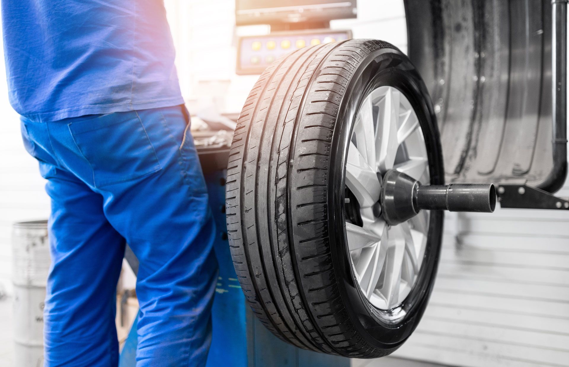 Mechanic balancing a car tire on a machine in a garage, wearing blue work pants and shirt