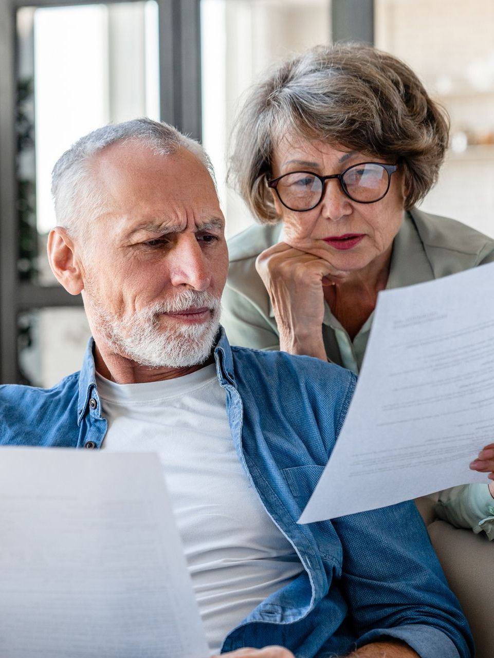 An elderly couple is sitting on a couch looking at a piece of paper.