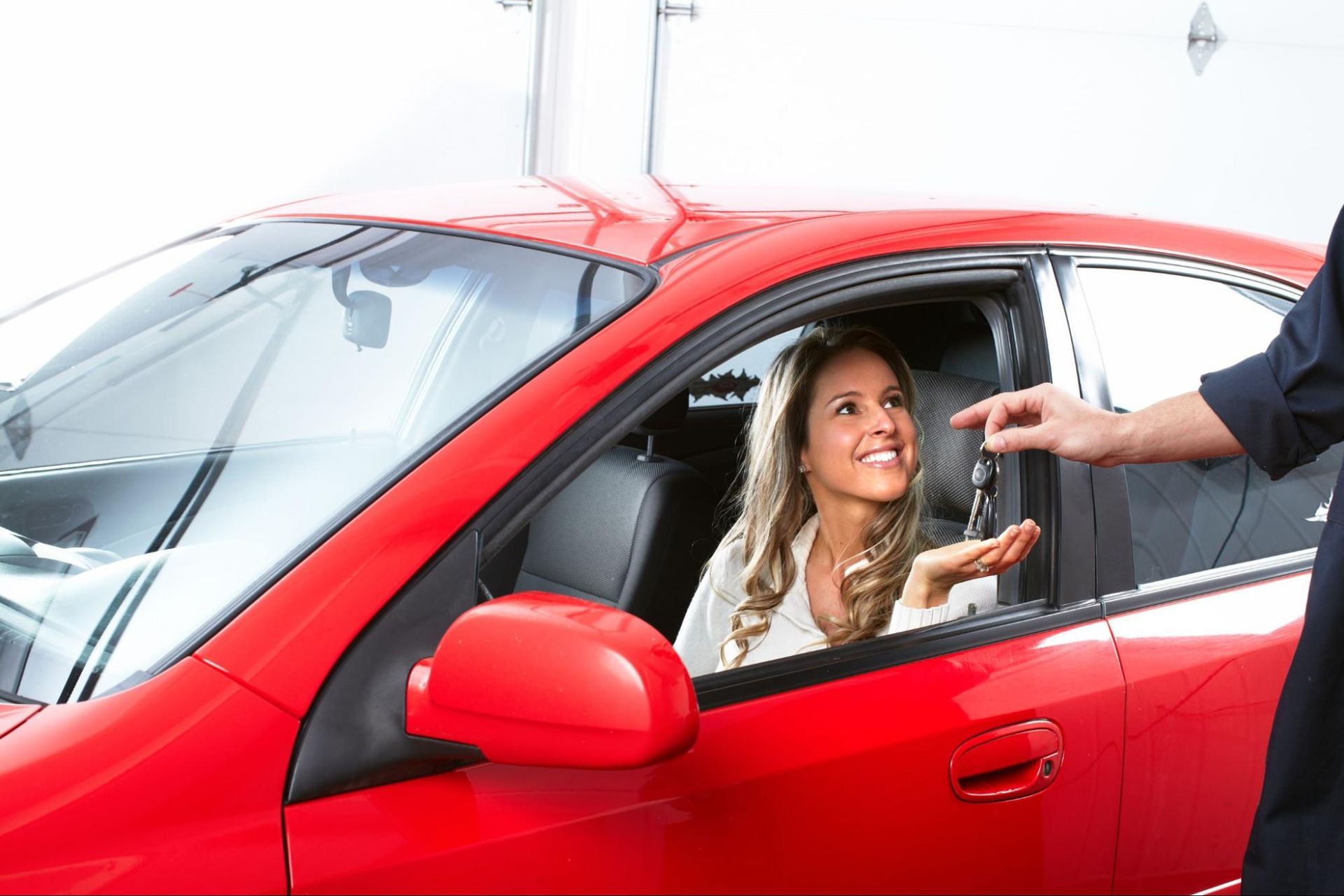 A woman is sitting in a red car while a man gives her the keys.